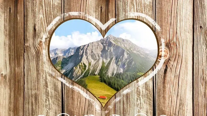 Holzwand mit einem herzförmigen Loch wodurch man Berg im Hintergrund erkennen kann